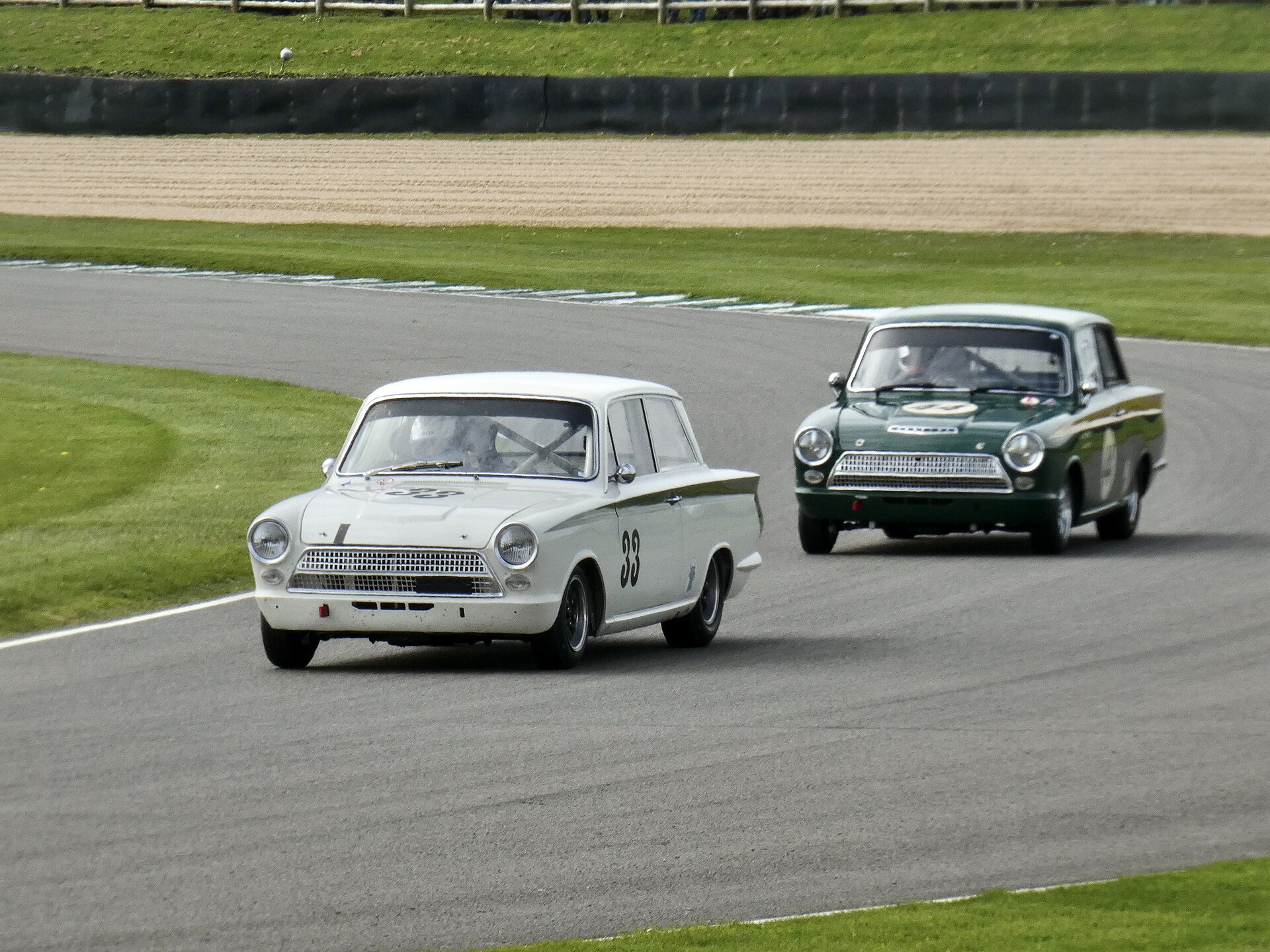 Lotus Cortinas racing at the Goodwood Members Meeting 2023, multiple cars in period livery sliding through a corner