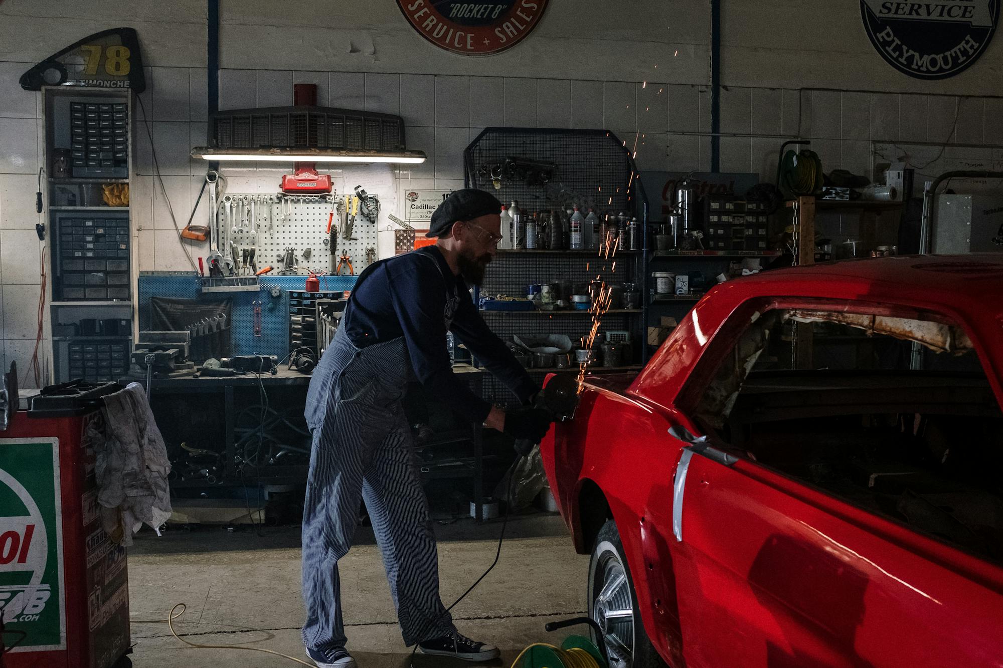 Mechanic grinding old paint and rust off a classic Ford during restoration — sparks flying in the workshop