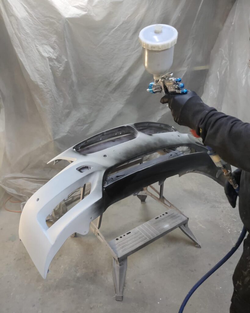 Bumper being primed with gravity-fed spray gun in booth at Top Touch Coachworks